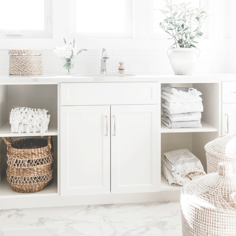 A light and airy image of a bathroom sink and baskets on white shelves