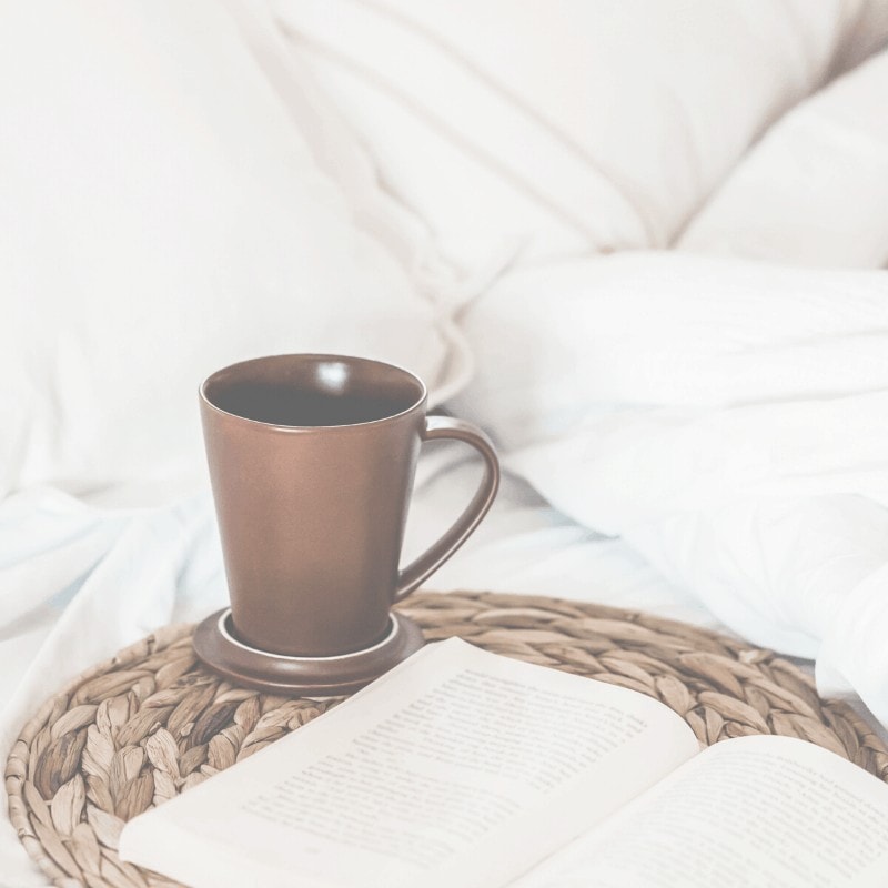 A woven mat sitting on a bed with a book and coffee cup on it.