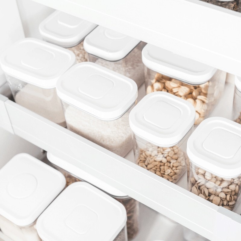 Minimalist pantry shelves with clear containers holding nuts and crackers.