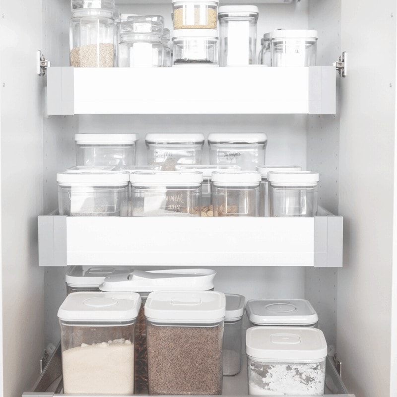 Clear containers on minimalist pantry shelves containing pantry staples.