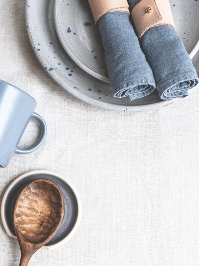 A wooden spoon, blue mug, stack of plates, and 2 blue napkins.
