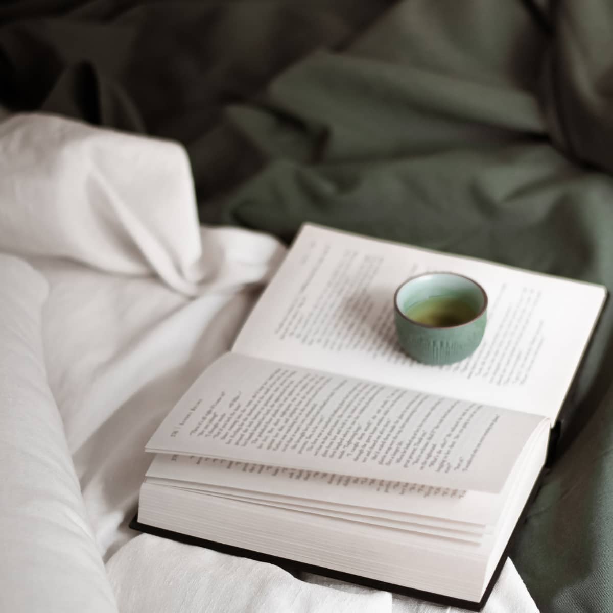 An open book and cup of tea laying on an unmade bed