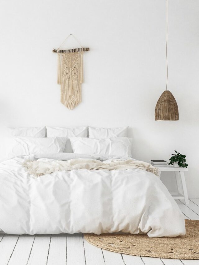 A minimalist bedroom with a white bedspread, tan throw rug, white cabinet and hanging lamp