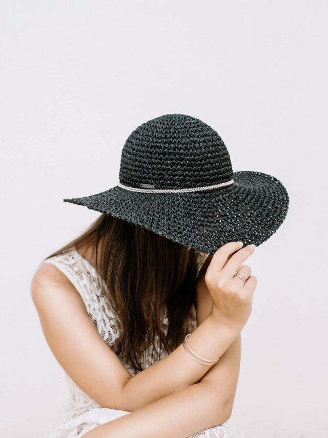 A woman pulling the brim of a black hat down over her face