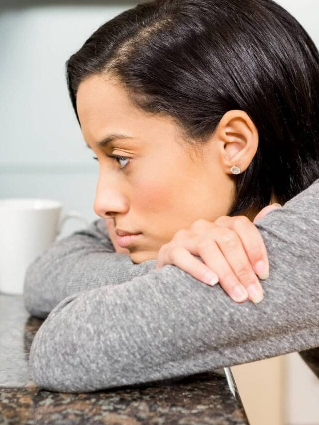 A sad looking lady leaning on the table in front of a laptop