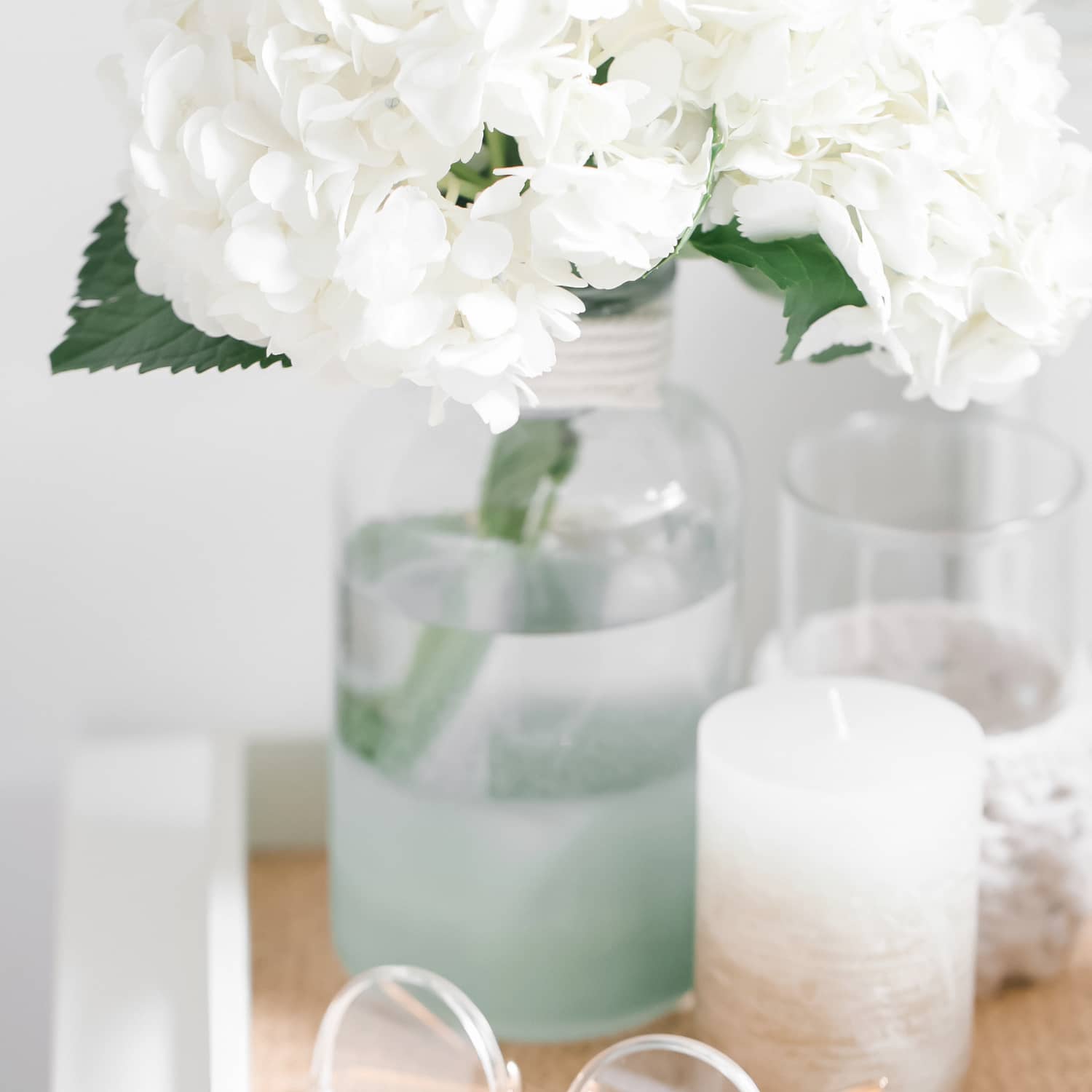 A tray holding a pair of glasses, a candle, and a vase holding white flowers.
