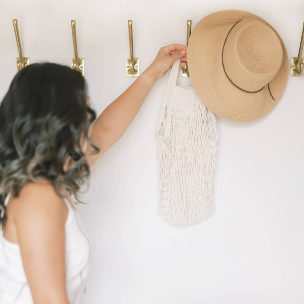 A woman reaching for a tan coloured hat that's hanging on a wall hook.