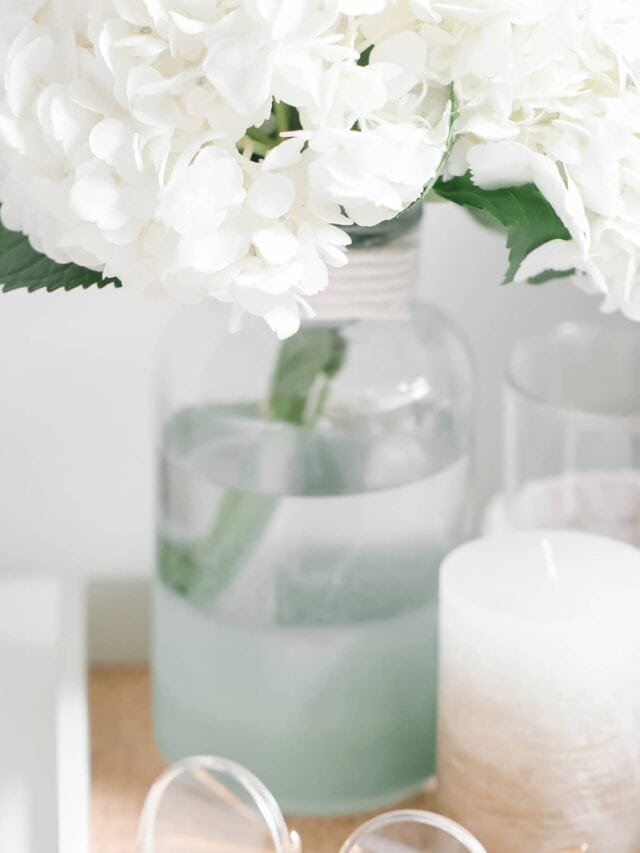 A tray holding a pair of glasses, a candle, and a vase holding white flowers.