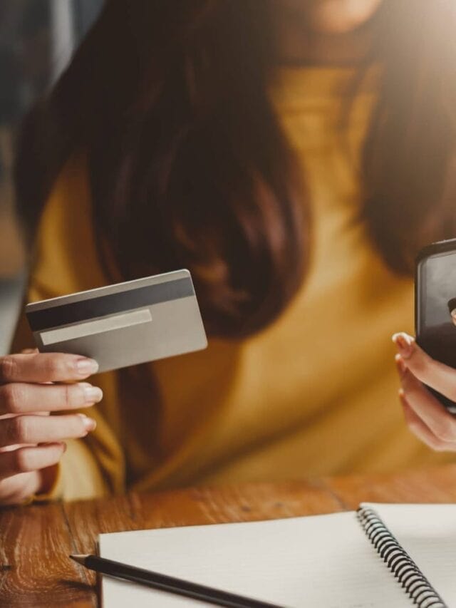A close up of a woman holding a credit card while looking at a cell phone.