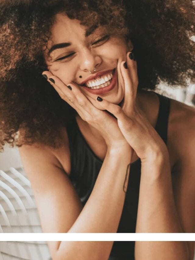 A woman with black curly hair wearing a black tank top smiling into the camera with a white frame overlay on the image.