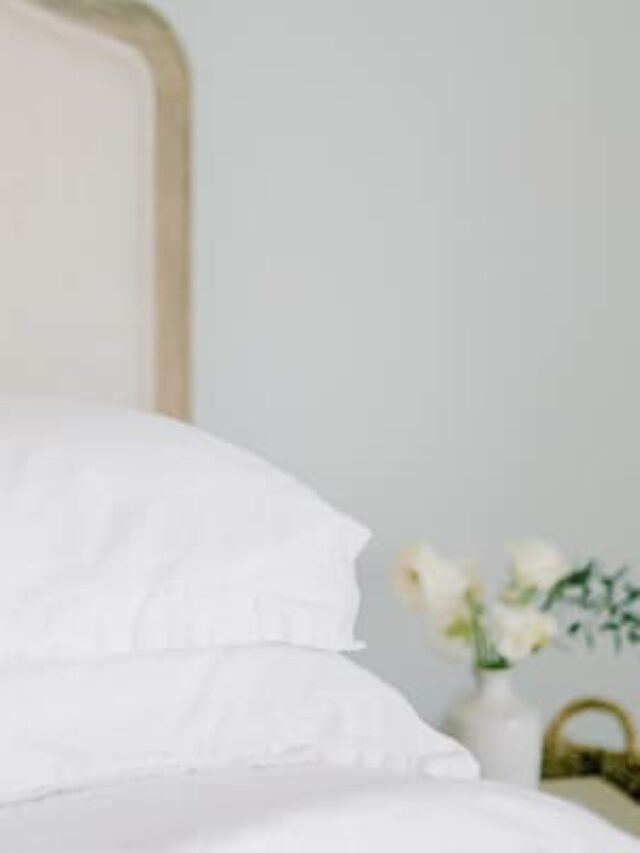 A bed with crisp white bedding, a vintage looking headboard, and a small vase on the side table.