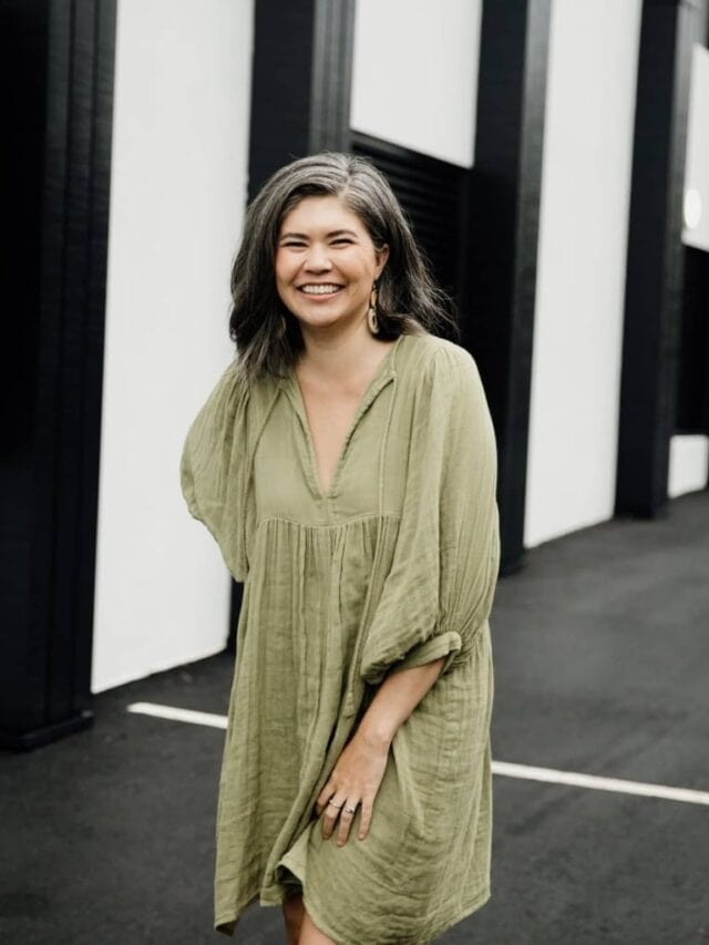 A woman wearing a green dress standing against a black and white wall smiling at the camera
