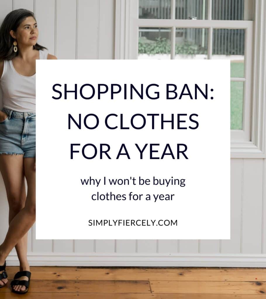 "Shopping Ban: No New Clothes for a Year why I won't be buying clothes for a year" in a white box with a woman wearing a white tank top, denim shorts, and sandals leaning against a white wooden wall looking towards a window in the background.