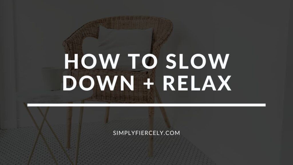 The words "How to Slow Down + Relax" on a translucent black background with an image of a wicker chair with a throw pillow on a tiled floor in the background