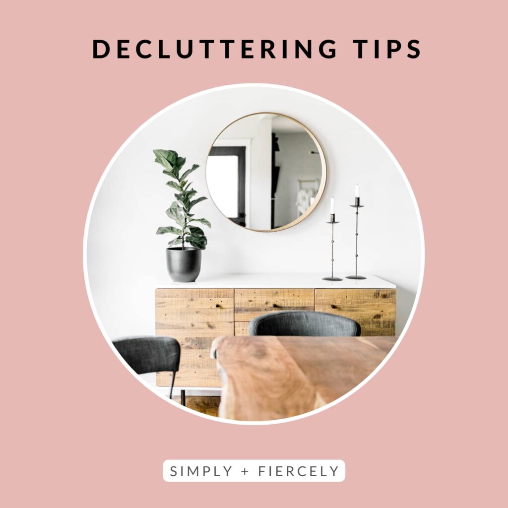 "Decluttering Tips" on a pink background with a round image of a dining room with a wooden buffet, a plant, 2 candle holders and a mirror in the background. There's a wood table and 2 grey chairs in the foreground.