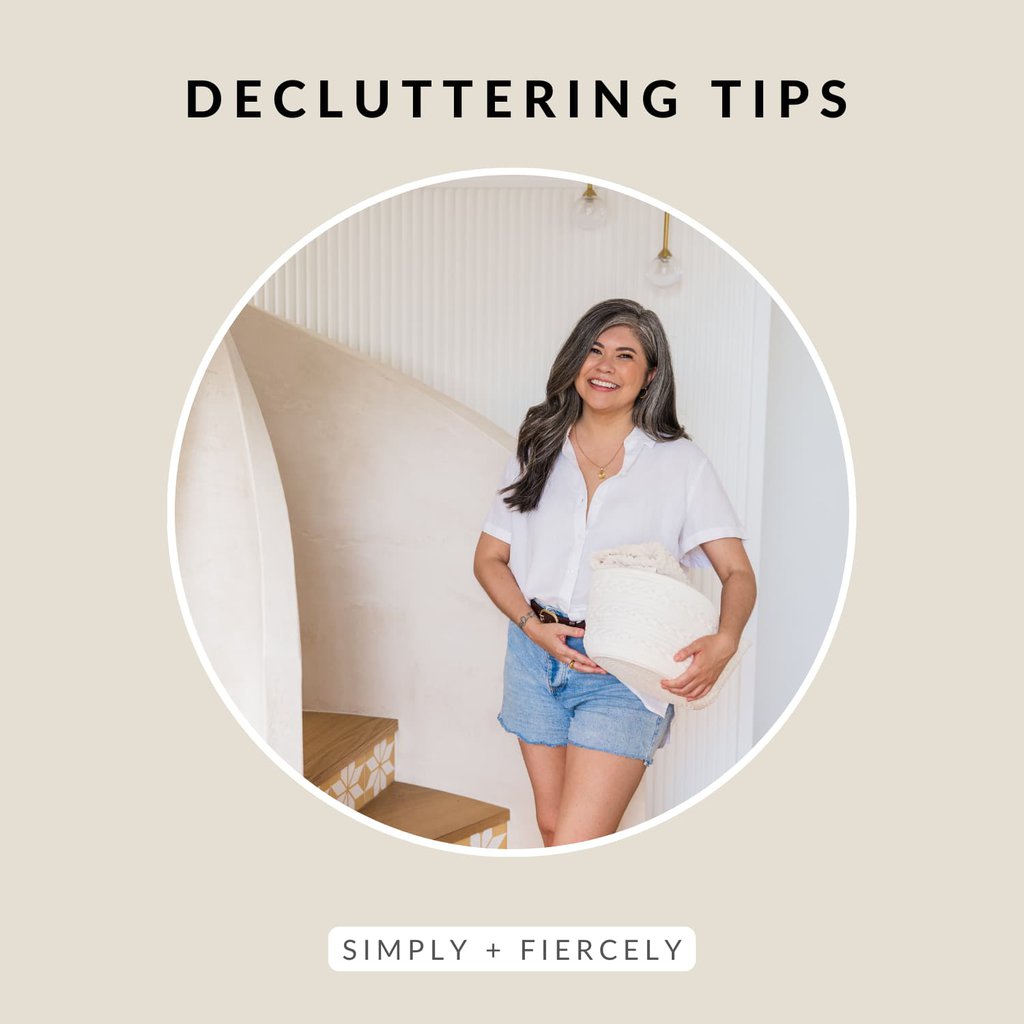 A round image of a smiling woman wearing denim shorts and a white button up top holding a basket of folded linen on a beige background with the words Decluttering Tips across the top.