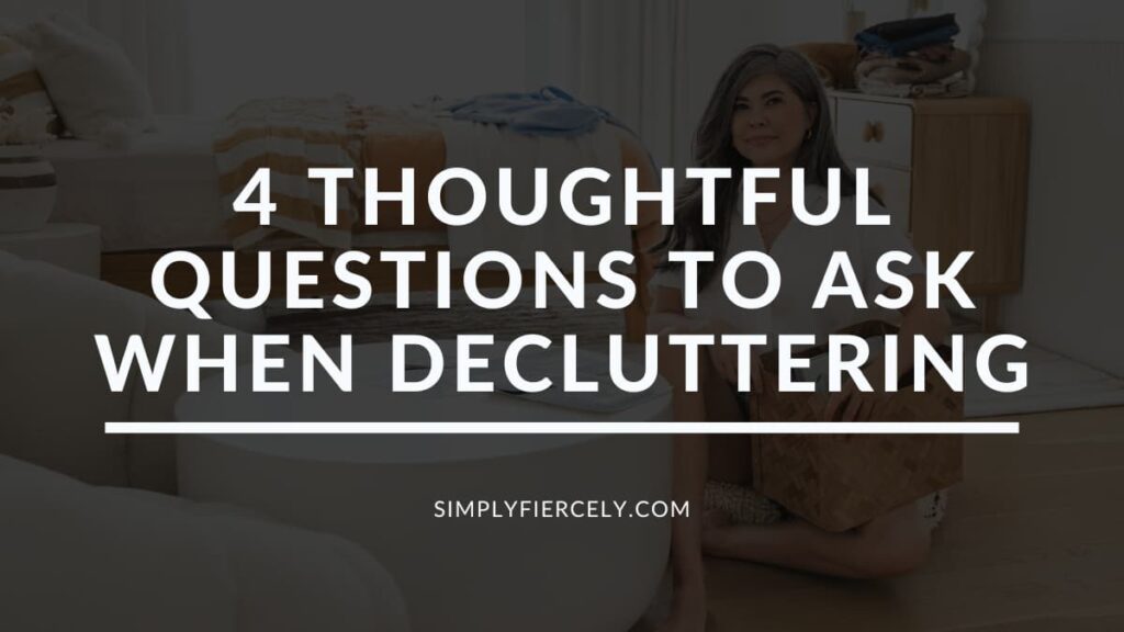 "4 Thoughtful Questions to Ask When Decluttering" in white letters on a translucent black overlay on top of an image of a smiling woman sitting on the floor holding a basket while decluttering a bedroom.