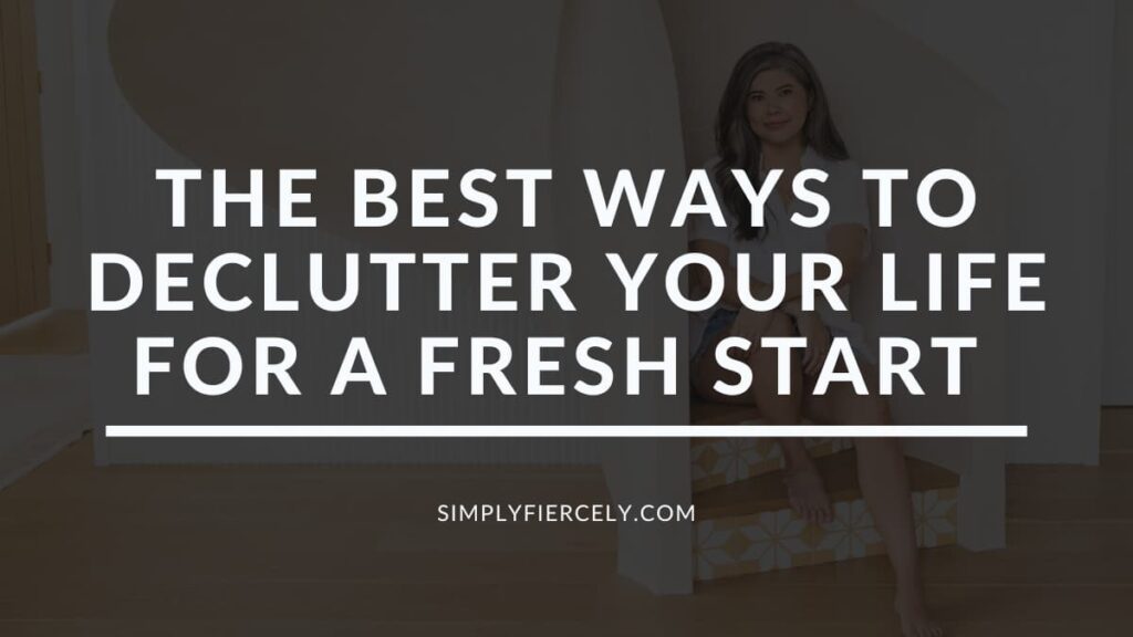 The words "The Best Ways To Declutter Your Life For A Fresh Start" on a translucent black overlay on top of an image of a smiling woman wearing denim shorts and a white button up top sitting on a spiral staircase in the background.