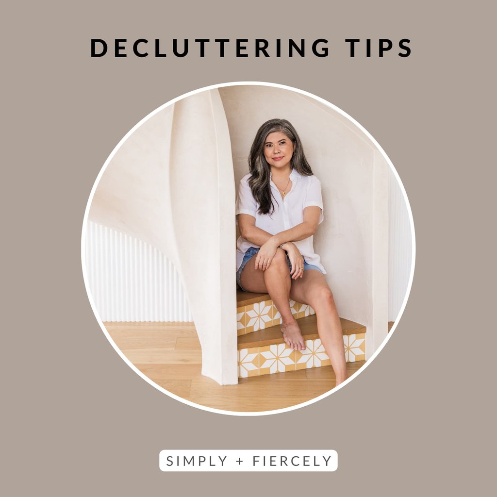 A round image of a smiling woman wearing denim shorts and a white button up top sitting on a spiral staircase on a taupe image with the words Decluttering Tips across the top