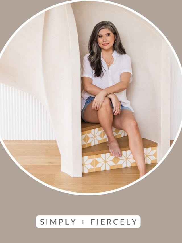 A round image of a smiling woman wearing denim shorts and a white button up top sitting on a spiral staircase on a taupe image with the words Decluttering Tips across the top