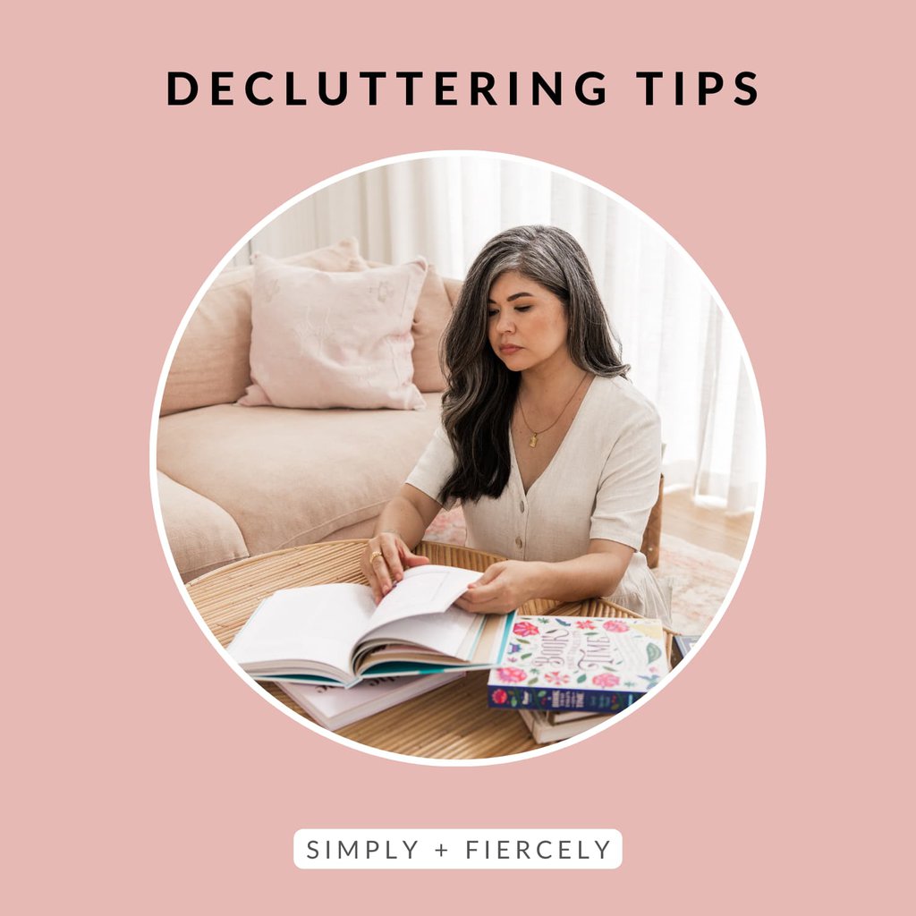 A round image of a woman sitting at a table on the floor in front of a sofa decluttering books on a pink background with the words Decluttering Tips across the top.