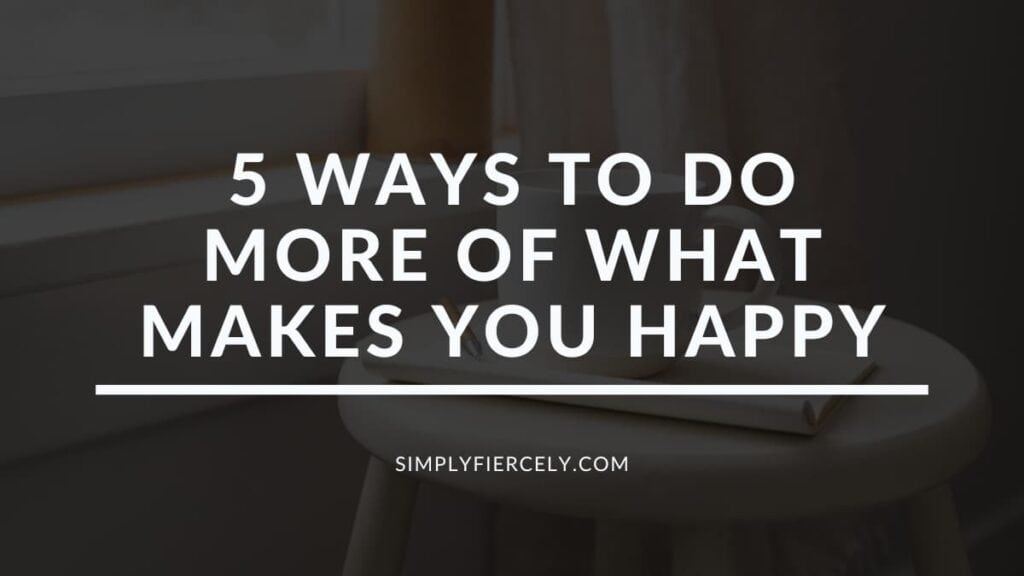 "5 Ways to Do More of What Makes You Happy" in white letters on a translucent black overlay on top of a close up image of a wooden stool in front of a window with a book and coffee mug on top.