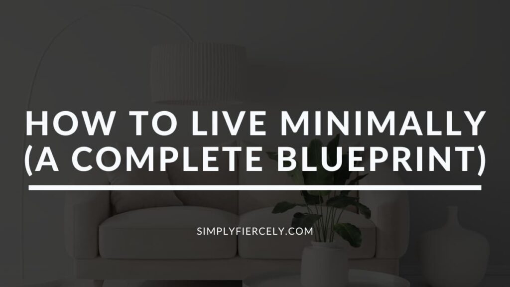 "How To Live Minimally (A Complete Blueprint)" in white letters on a translucent black overlay on top of an image of a minimalist living room with a cream coloured sofa, and a plant in a white vase on a white table with a hanging white lamp overhead.