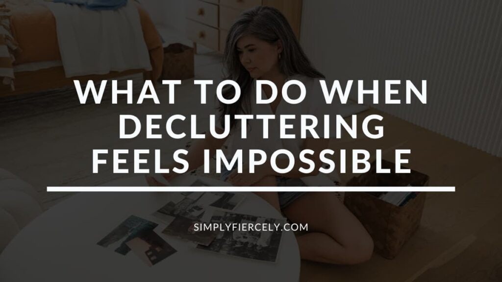 "What to Do When Decluttering Feels Impossible" in white letters on a translucent black overlay on top of an image of a woman sitting on a hardwood floor in a bedroom decluttering pictures.