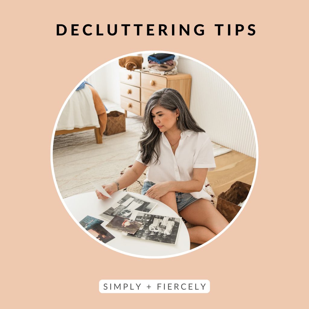 A round image of a woman sitting on a hardwood floor in a bedroom decluttering pictures on an orange background with the words Decluttering Tips across the top.
