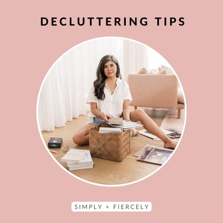 A round image of a woman wearing shorts and a white button up top smiling at the camera while sitting on the floor decluttering a basket on a pink background with the words Decluttering Tips across the top.